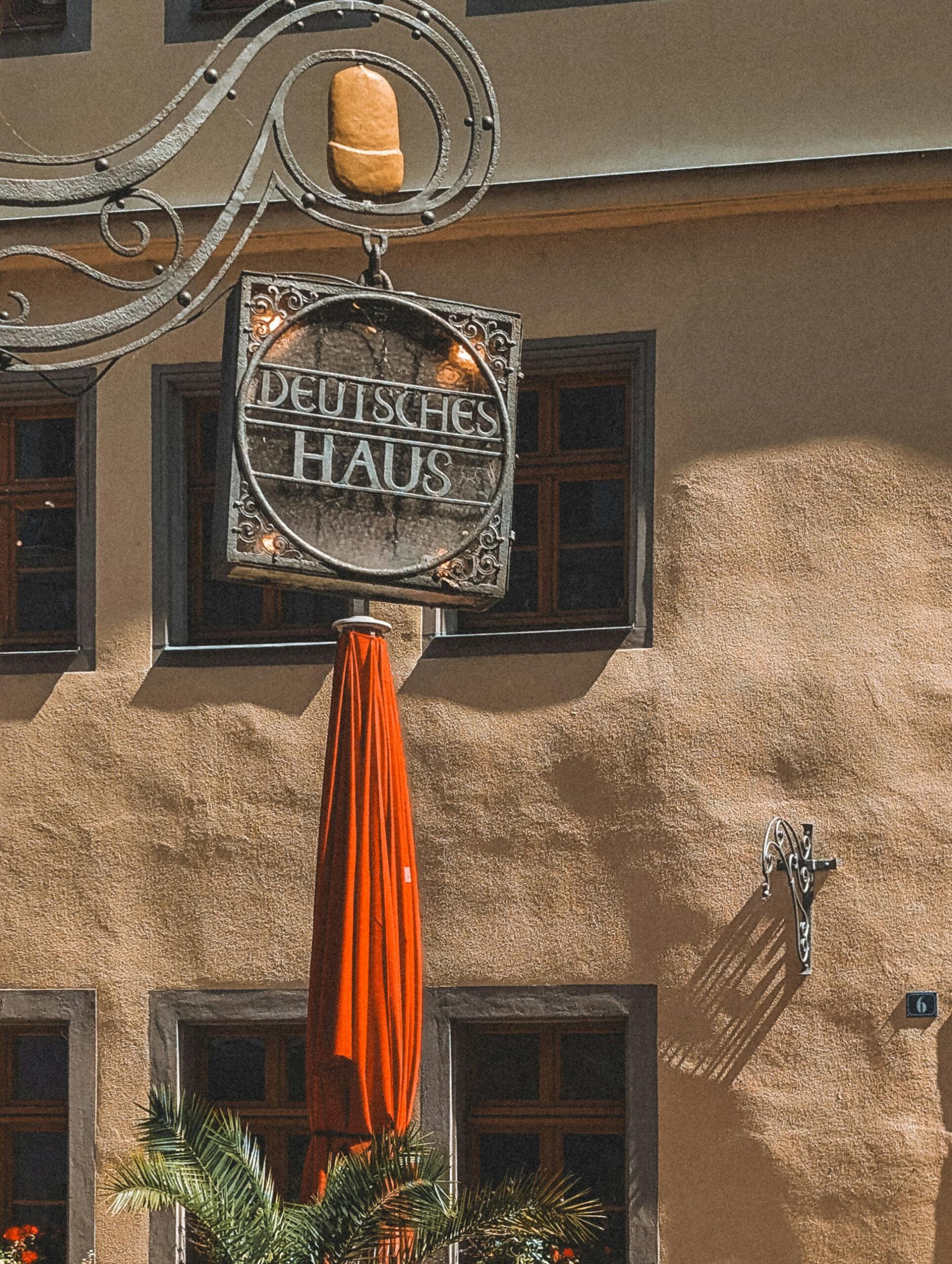 Rustic sign of Deutsches Haus with vibrant umbrella in Pirna, Saxony, Germany.
